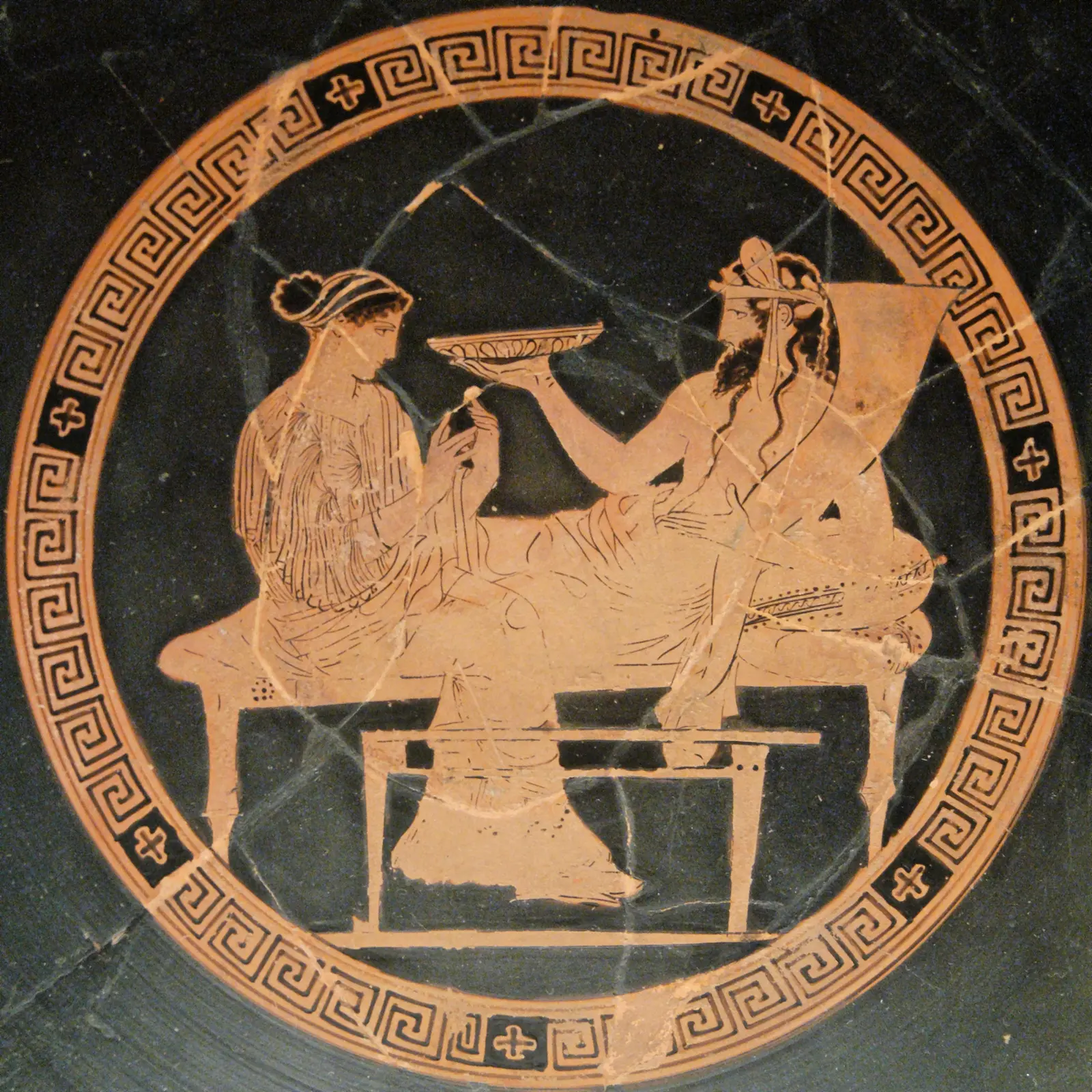 Persephone sits at the foot of a couch facing Hades, who reclines with a shallow dish, on a red-figure cup of 440–430 BC