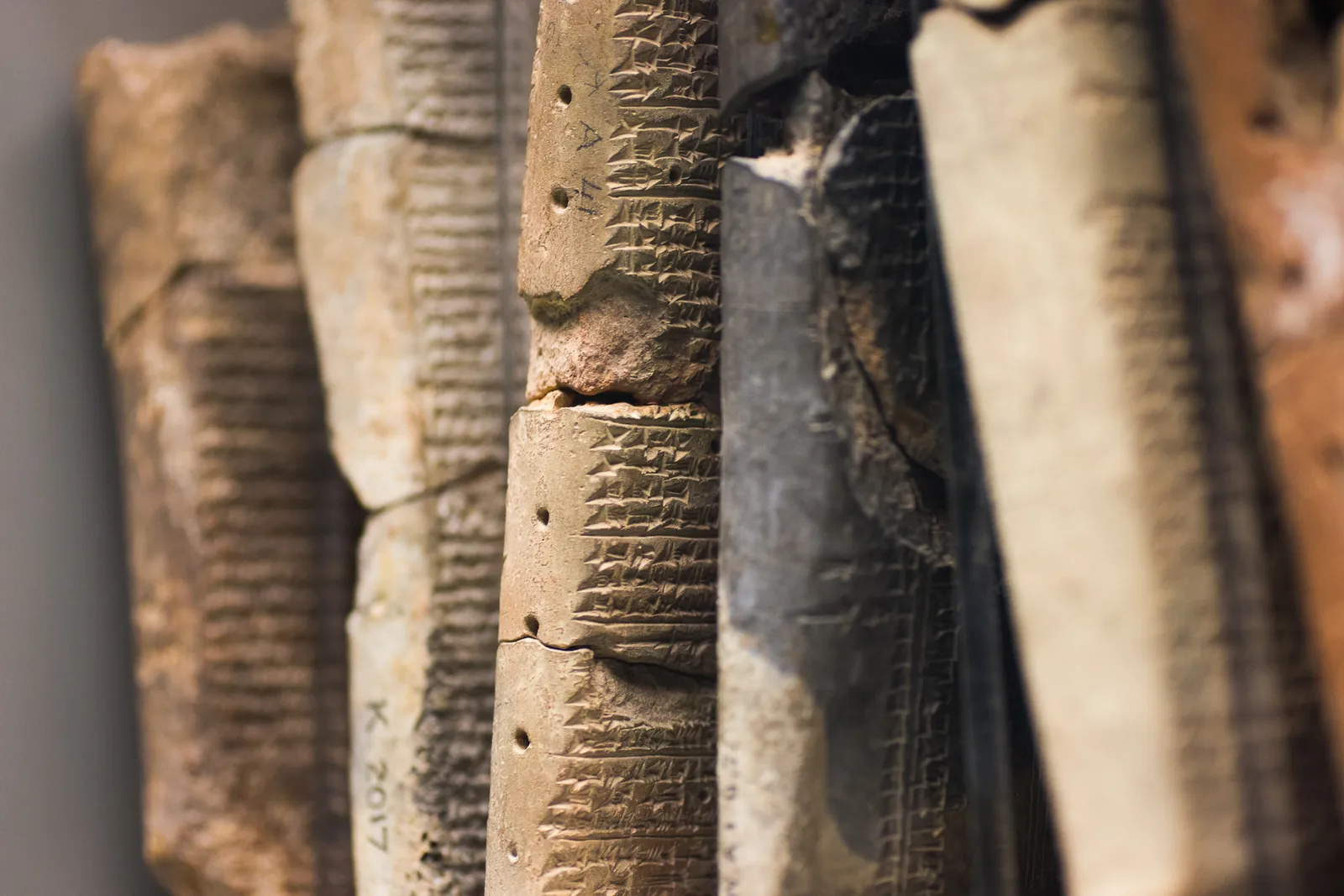 Close-up of clay tablets standing on edge, rows of wedge-shaped signs on their sides, one marked K. 2017