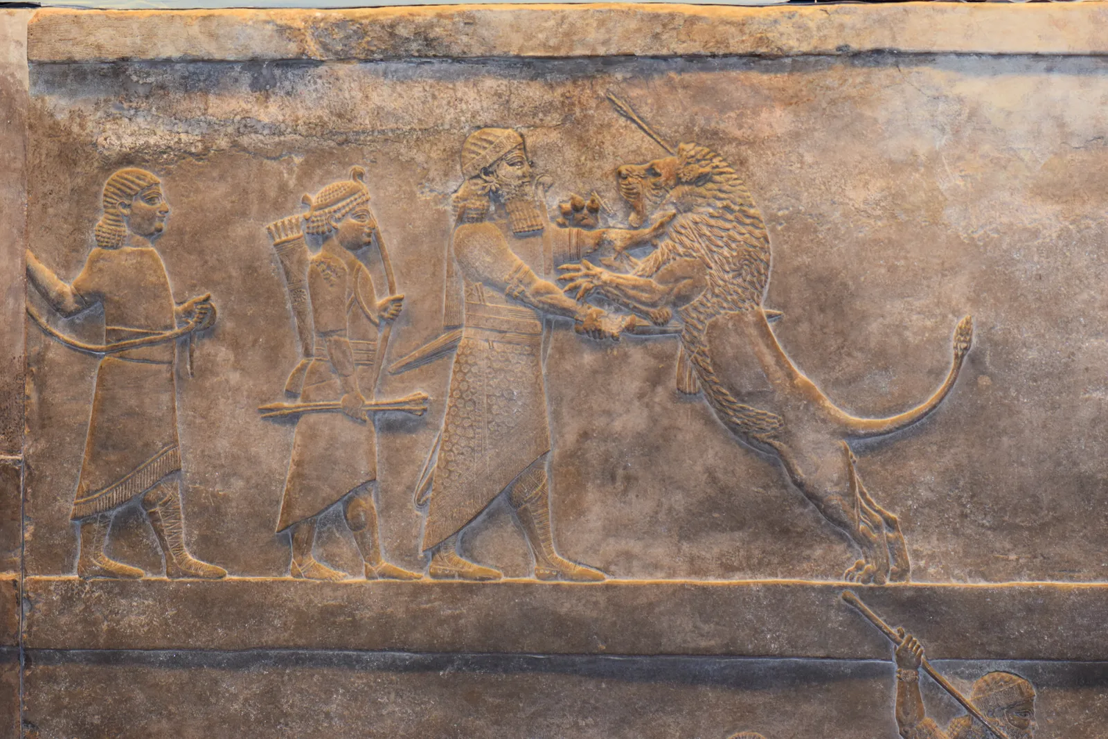 Ashurbanipal's lion hunt relief: the Assyrian king grips a rearing lion while two attendants follow